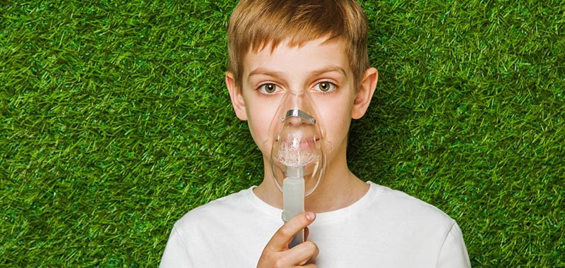 Portrait of a boy breathing through inhaler mask over spring green grass background