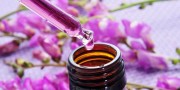 closeup of a dropper bottle and a pile of purple flowers on a purple background